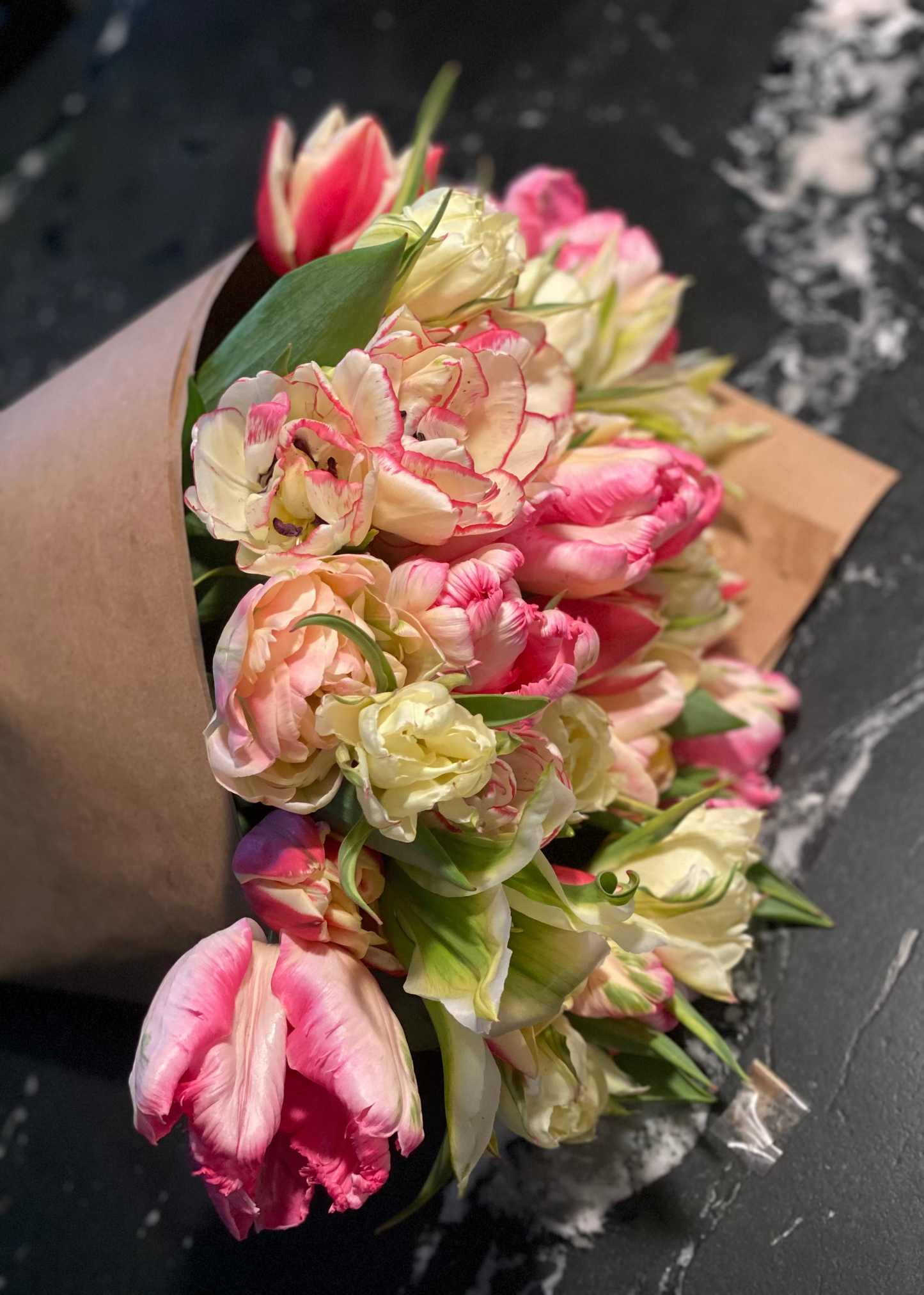 Bouquet of pink and white tulips wrapped in brown paper on a dark surface