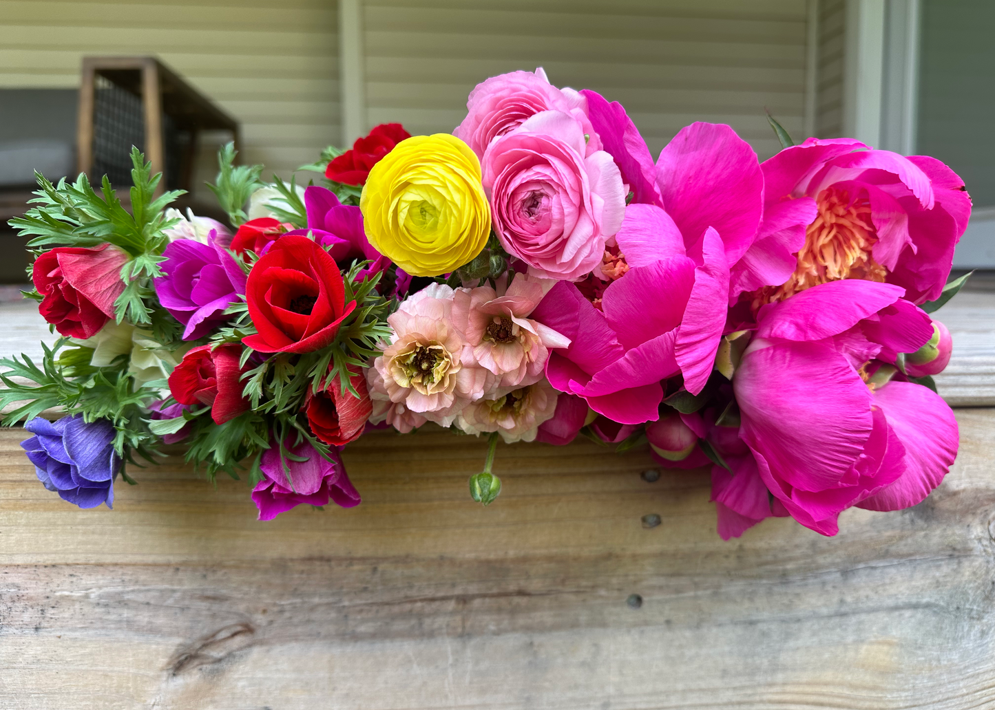 Locally grown anemones, ranunculus, and peony flowers set on a porch outside.