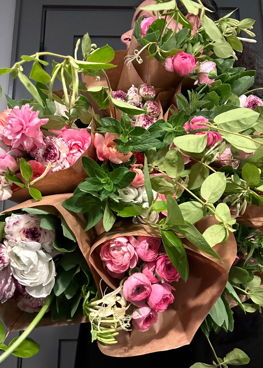 Bouquets of locally grown pink and white flowers wrapped in brown paper held by the farmer against a dark background.
